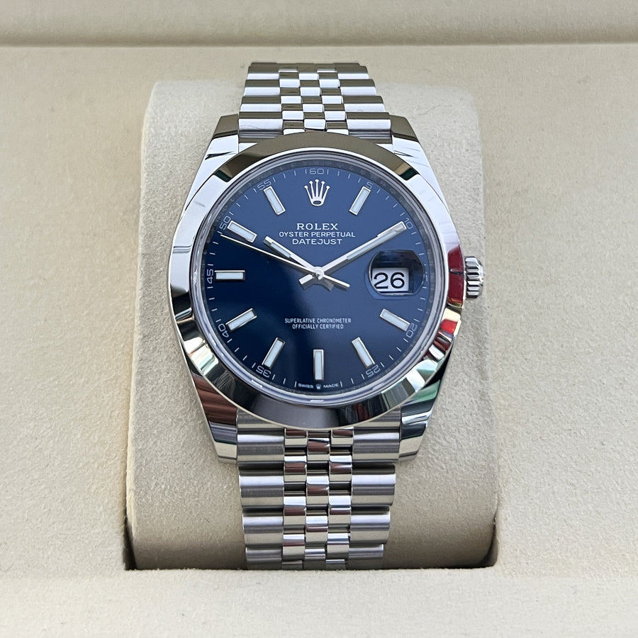 Rolex watch with blue face and silver bracelet on a beige cushion