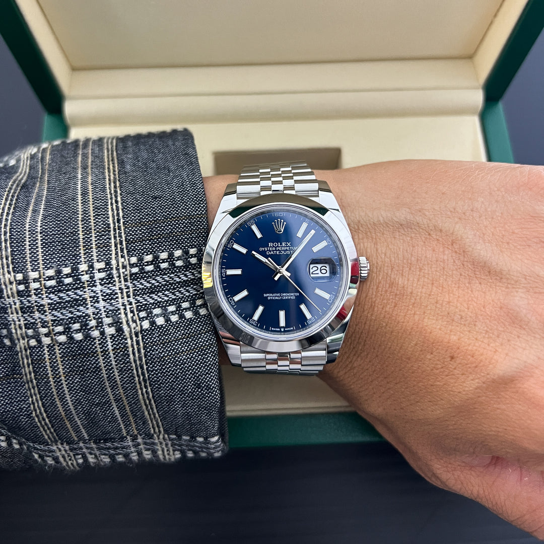 Person wearing a silver watch with a blue face on a wrist, with a box in the background.