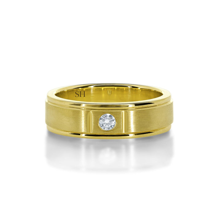 Men's satin finish diamond wedding band with grooves to edges R12-002B-W0074. This classic 18k white gold men's wedding band has been centrally hammer set with a round brilliant cut diamond. The subtlety of the diamond is enhanced with an all over satin finish. The ring has an extra thickness and weight to it and has a uniform width. Although the profile of this ring is flat